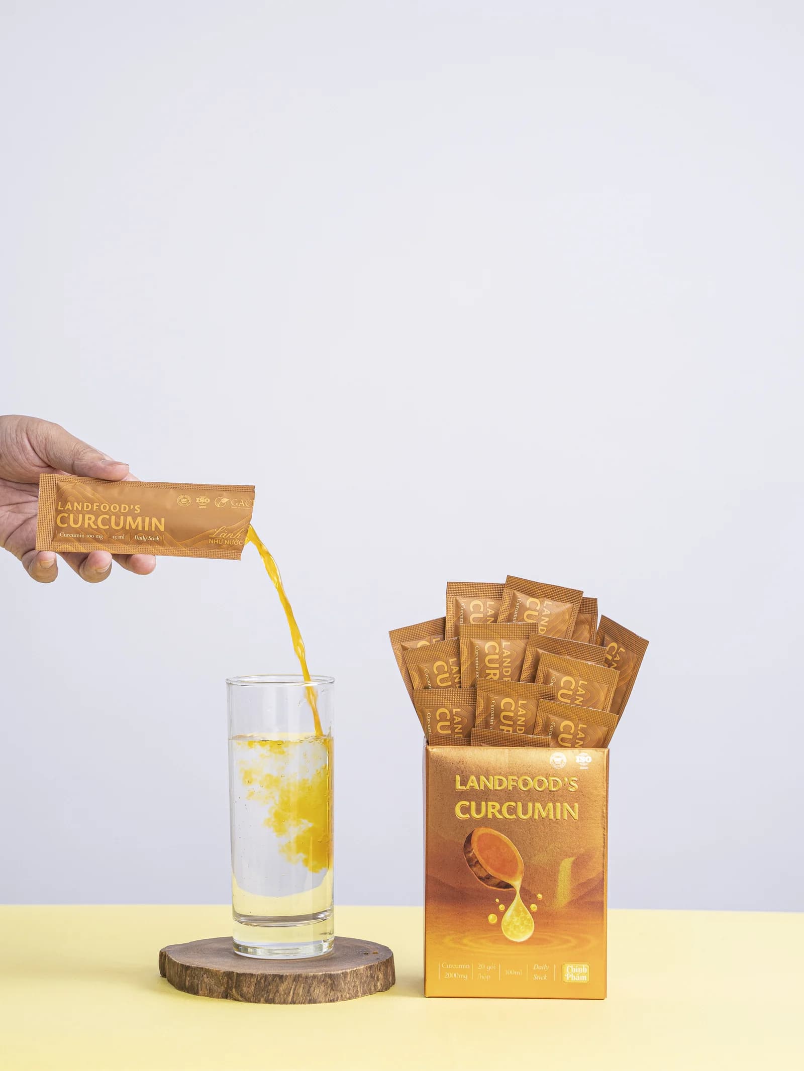Gói LANDFOOD'S Curcumin dạng nước được rót vào ly bên cạnh hộp sản phẩm